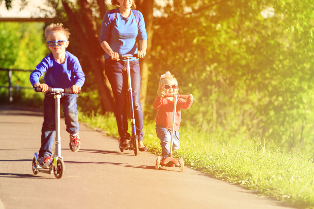 mother with kids riding scooters in summer